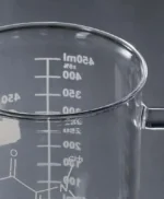 Beaker with measurement markings for science experiments, made of clear glass with a handle, ideal for educational demonstrations and science decor.