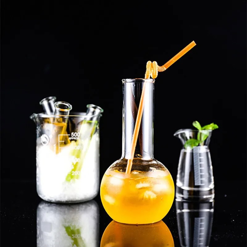 Science Gadgets | Science Decor & Educational Toys Shop Beaker with yellow liquid and straw, laboratory glassware with scientific liquids, and a small plant in a beaker on a black background.