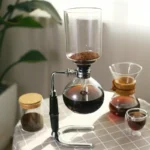 Laboratory coffee brewing setup with glass apparatus, including a siphon coffee maker, beakers, and containers, demonstrating the science of coffee extraction and brewing techniques.