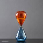 A sleek, modern hourglass with orange and blue glass bulbs, perfect for educational demonstrations and stylish home or office decor.