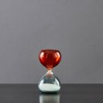 An elegant glass hourglass with a red top and white sand inside, perfect for science decor and educational purposes.
