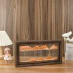 Miniature sand dunes model inside a wooden framed glass display case, showcasing layered orange and beige sands, placed on a wooden surface with decorative items around.