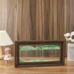 Miniature landscape diorama inside a glass display case with green hills and a wooden frame, placed on a wooden surface.
