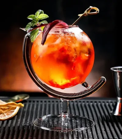 A vibrant tropical cocktail served in a glass with a metal stand, garnished with a mint sprig and a slice of fruit, perfect for a refreshing summer drink.