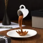 White coffee mug with a spill-shaped design pouring chocolate or coffee onto a white plate, creating a realistic spill effect.