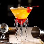 Elegant cocktail served in a glass with a unique tentacle-shaped stand, garnished with a cherry and ice cubes, perfect for science-themed decor or educational displays.