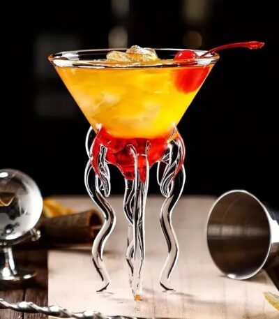 Elegant cocktail served in a glass with a unique tentacle-shaped stand, garnished with a cherry and ice cubes, perfect for science-themed decor or educational displays.
