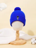 Bright blue knit beanie with a small astronaut patch, featuring a pom-pom on top, displayed on a mannequin head against a neutral background. Perfect for winter and casual wear.