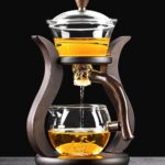 Elegant glass tea infuser with wooden handle and metal frame, showcasing brewing tea with golden liquid. Perfect for tea enthusiasts and educational demonstrations.