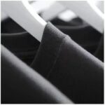 Close-up of a black T-shirt hanging on a white hanger in a closet, showcasing fabric texture and neat organization.