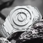 Modern silver wristwatch with a sleek, futuristic design and metallic finish, resting on a textured rock surface.