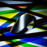 Modern black computer mouse placed on a vibrant, colorful geometric background with intersecting lines and shapes, highlighting technology and design.