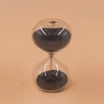 Clear glass sand timer with black sand, demonstrating the passage of time, ideal for science education and decor.