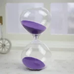 Clear glass hourglass with flowing purple sand, showcasing a classic time-measuring device perfect for educational and decorative purposes.
