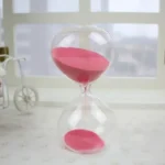 Bright pink sand flowing through a transparent glass hourglass timer.