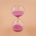 Transparent hourglass with pink sand flowing between the chambers, symbolizing the passage of time.