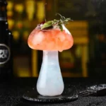A creative cocktail served in a glass shaped like a mushroom, garnished with fresh herbs and a cherry on top. Perfect for science-themed decor or educational displays.