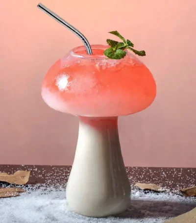Mushroom-shaped beverage with pink foam, mint garnish, and metal straw on a pink background.