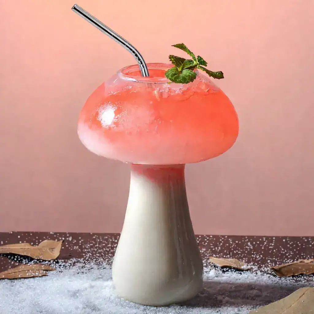 Mushroom-shaped beverage with pink foam, mint garnish, and metal straw on a pink background.