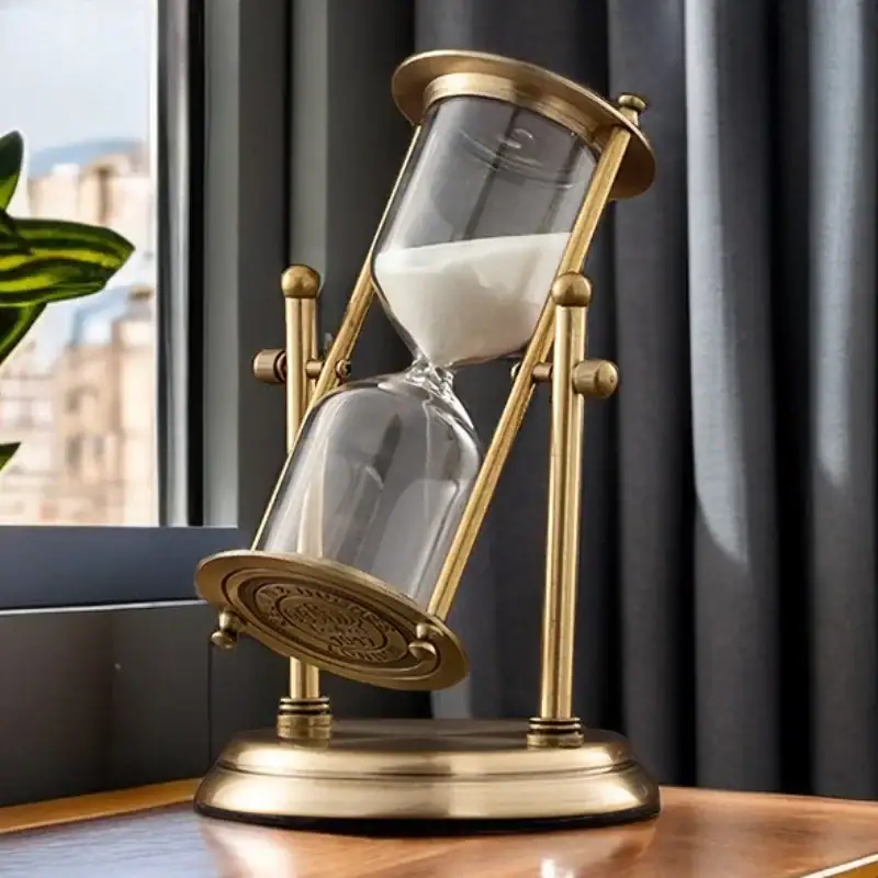 Sand Timer with Gold Frame Elegant sand timer with a gold frame and glass body, filled with white sand, placed on a wooden surface near a window.
