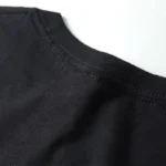 Close-up of a plain black crew neck T-shirt fabric, showing the neckline and smooth texture.
