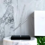 Sleek metallic sculpture featuring intersecting rods on a black base, ideal for contemporary interior decoration and adding an artistic touch to living spaces.