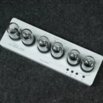 A white power strip with six shiny metallic sockets arranged in a row, designed for educational science gadgets and experiments, placed on a dark textured surface.