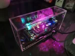 Modern digital LED clock housed in a clear acrylic case, showcasing the internal electronic components and colorful LED display.