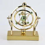 Atomic model desk decor with gold and green spheres representing electrons and nucleus, mounted on a rectangular gold base. Perfect for science enthusiasts and educational settings.