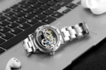 Elegant skeleton watch showcasing intricate internal gears and mechanisms, placed on a laptop keyboard with wireless earbuds nearby.