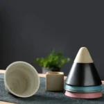 Stacked colorful and black-and-white cone-shaped bowls with a small beige cube and a white bowl on a dark surface.