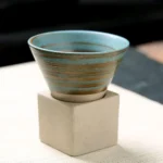 Small ceramic bowl with blue and brown glaze, placed on a concrete cube, ideal for decorative or educational purposes.