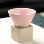 Small pink ceramic bowl placed on a concrete cube, showcasing modern minimalist design with smooth surface and subtle color.