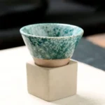A small ceramic bowl with a textured turquoise glaze, displayed on a white cube pedestal. Perfect for science-inspired decor or educational demonstrations.