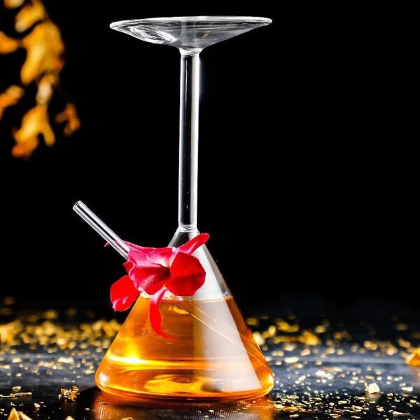 Erlenmeyer flask with a glass stirring rod and a glass dish balanced on top, filled with a yellow-orange liquid, set against a black background with scattered gold particles.