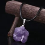 Beautiful purple amethyst crystal pendant on a black cord necklace, displayed against a dark background with a wooden stand.