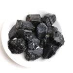 Raw black tourmaline crystals on a white background, showcasing their natural, rugged texture and deep black color, ideal for metaphysical healing and protection.