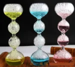 Vibrant glass hourglasses filled with bubbling colored liquids in yellow, blue, and pink, displayed against a black background.