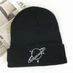 A black knit beanie featuring a white embroidered planet with rings and surrounding stars, perfect for space enthusiasts and casual wear.