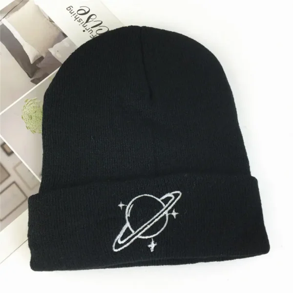 A black knit beanie featuring a white embroidered planet with rings and surrounding stars, perfect for space enthusiasts and casual wear.
