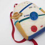 Bright children's backpack featuring space-themed patches of planets and stars, perfect for young explorers and students.