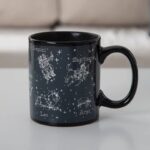 Black ceramic mug featuring white zodiac constellation illustrations of Gemini, Sagittarius, Leo, and Aries with their names, set against a starry background.