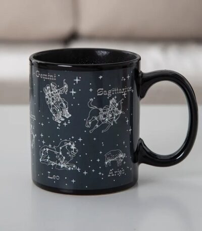 Black ceramic mug featuring white zodiac constellation illustrations of Gemini, Sagittarius, Leo, and Aries with their names, set against a starry background.