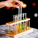 Hand holding a test tube with colorful liquids in a laboratory setting, showcasing a science experiment with test tubes and a wooden rack.