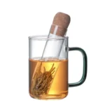 A glass mug with a tea infuser containing tea leaves and a test tube with a cork stopper, demonstrating a science-themed beverage preparation.