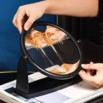 Hands holding a circular mirror demonstrating the reflection of colorful sand flowing inside, showcasing a science experiment or decorative science display.