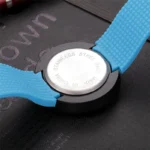Close-up of a wristwatch with a stainless steel back and blue silicone strap, resting on a textured surface.