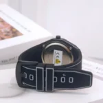 Close-up of a modern smartwatch with a black strap and digital interface, placed on a white surface with a blurred background.
