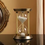 Classic hourglass sand timer with white sand, decorative gold and black frame, ideal for home decor and educational purposes.