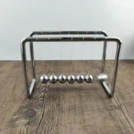 Metal Newton's Cradle with six swinging balls on a wooden surface, demonstrating conservation of momentum and energy.